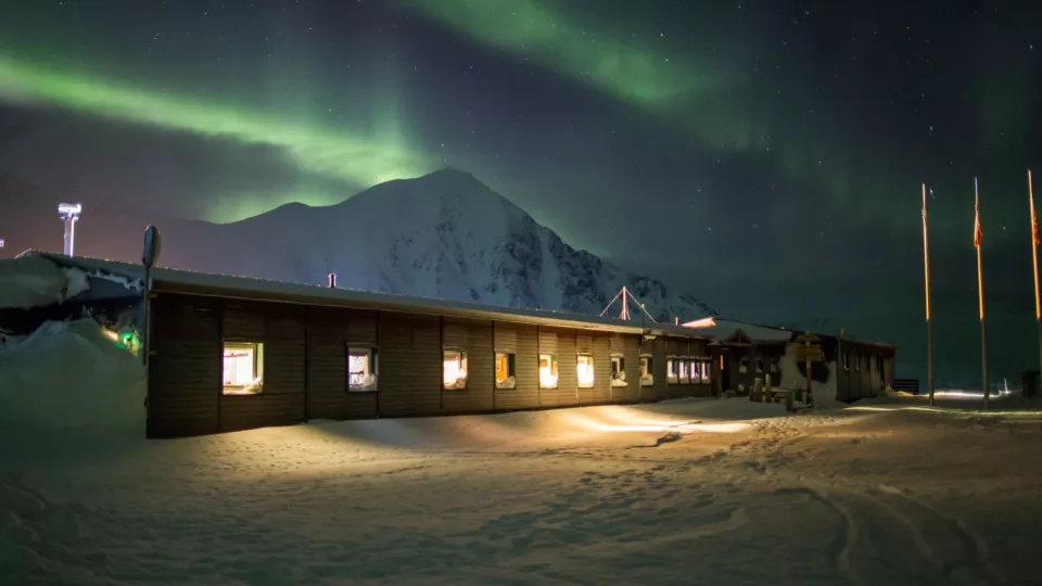 Arctic station house in snow covered ground, with northern lights in the dark sky. Photo.
