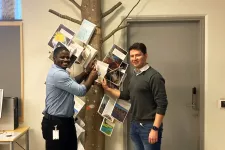 Two people nailing a thesis to a tree trunk installed in a library